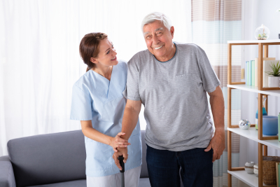 emale Caretaker Assisting Happy Senior Man While Walking At Home