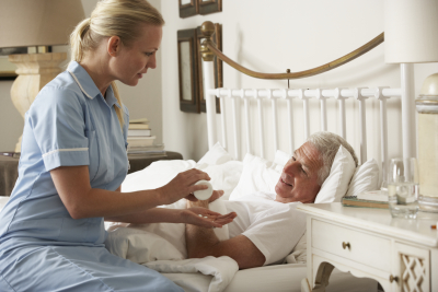 urse Giving Senior Male Medication In Bed At Home