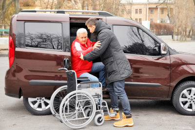 Young man helping handicapped man to sit in wheelchair