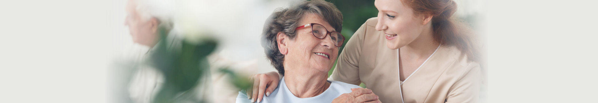 Professional helpful caregiver comforting smiling senior woman at nursing home